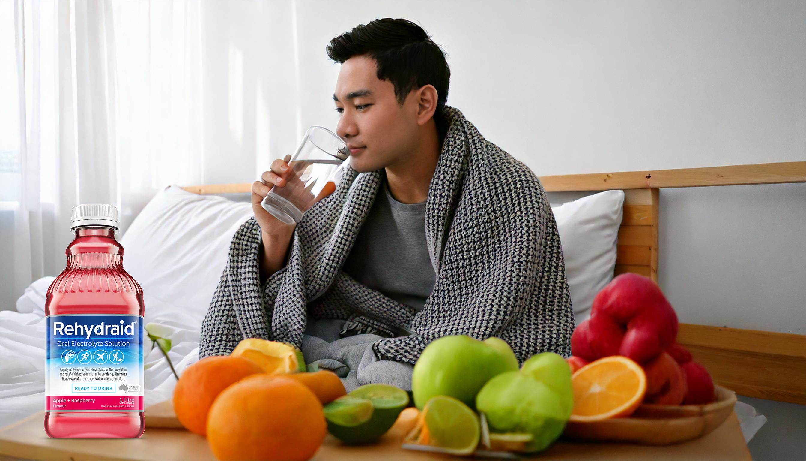 Person recovering from illness, drinking water with Rehydraid products on a bedside table, surrounded by fresh fruits like oranges, raspberries and apples